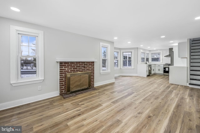 unfurnished living room with light wood-type flooring, a brick fireplace, a wealth of natural light, and sink