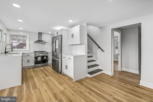 kitchen featuring white cabinets, wall chimney range hood, sink, light hardwood / wood-style flooring, and appliances with stainless steel finishes