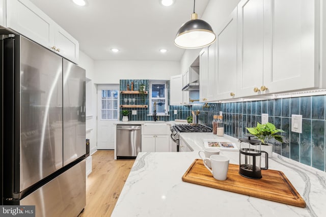 kitchen with decorative light fixtures, light stone counters, white cabinetry, and appliances with stainless steel finishes