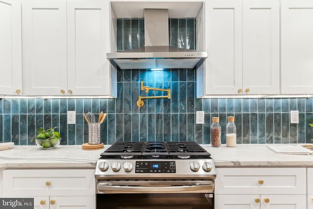 kitchen with backsplash, stainless steel range with gas cooktop, white cabinetry, and wall chimney exhaust hood