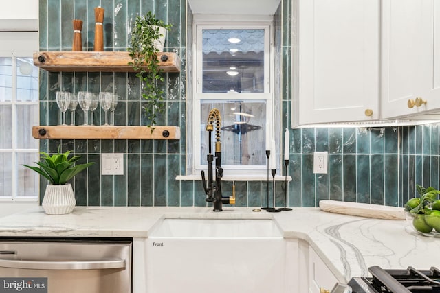 interior space with stainless steel dishwasher, light stone countertops, white cabinetry, and sink