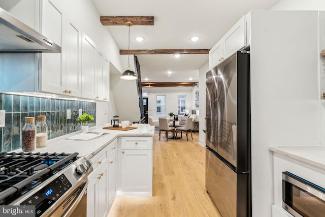 kitchen with white cabinetry, wall chimney range hood, hanging light fixtures, and appliances with stainless steel finishes