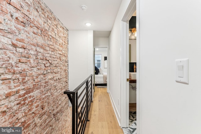 hall featuring light wood-type flooring and brick wall