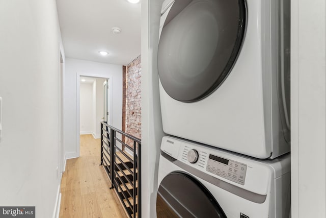 washroom with light hardwood / wood-style floors, stacked washing maching and dryer, and brick wall