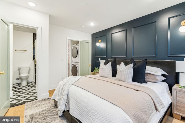 bedroom with light wood-type flooring, stacked washer and dryer, and ensuite bath