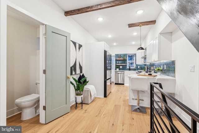 kitchen featuring kitchen peninsula, appliances with stainless steel finishes, decorative light fixtures, beamed ceiling, and white cabinetry