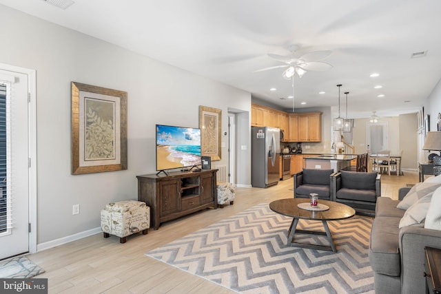 living room with light hardwood / wood-style floors, ceiling fan, and sink