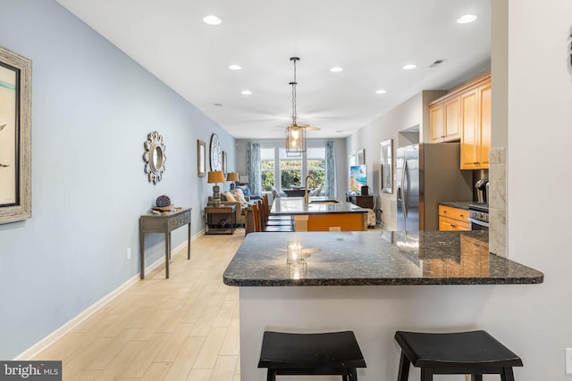 kitchen featuring ceiling fan, a kitchen breakfast bar, stainless steel refrigerator with ice dispenser, kitchen peninsula, and light hardwood / wood-style floors