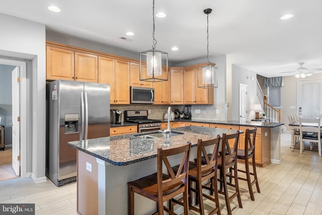 kitchen featuring a breakfast bar area, dark stone countertops, a kitchen island with sink, and stainless steel appliances