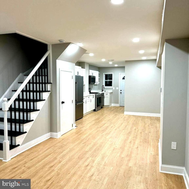 kitchen with sink, stainless steel appliances, white cabinetry, and light wood-type flooring