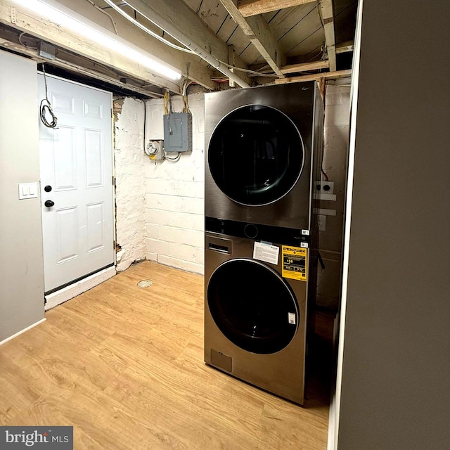 clothes washing area featuring electric panel, light hardwood / wood-style flooring, and stacked washer / drying machine