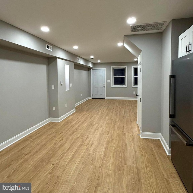 basement with stainless steel refrigerator and light hardwood / wood-style flooring