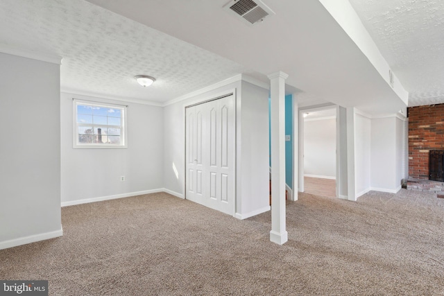 basement featuring carpet flooring, ornamental molding, a textured ceiling, and a brick fireplace