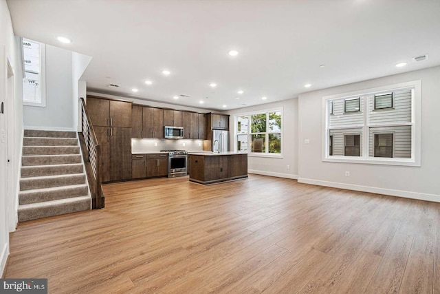 kitchen featuring light wood-type flooring, dark brown cabinetry, stainless steel appliances, sink, and a center island with sink