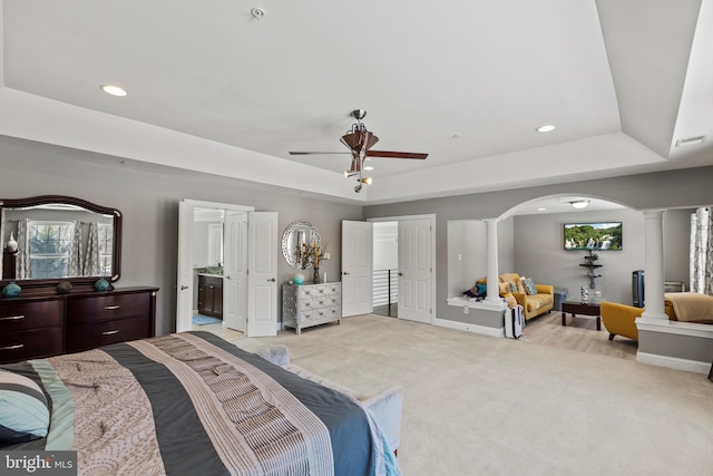 bedroom featuring a raised ceiling, connected bathroom, decorative columns, ceiling fan, and light carpet