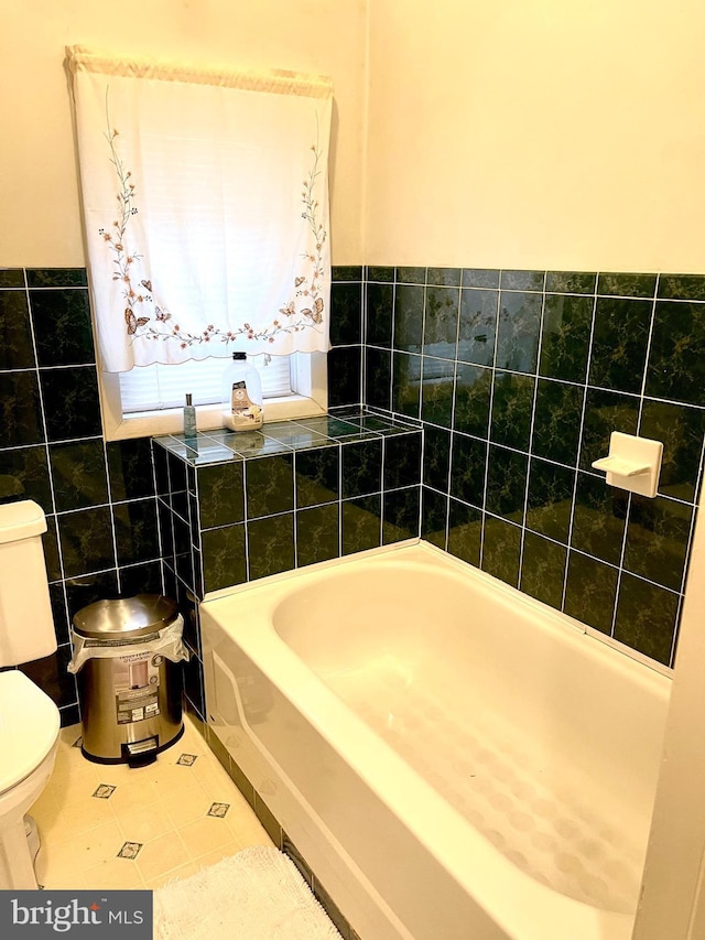 bathroom featuring tile patterned flooring, toilet, a tub, and tile walls