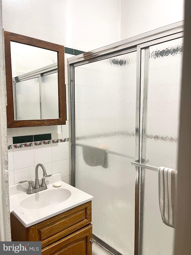 bathroom featuring vanity, a shower with door, tile walls, and tasteful backsplash