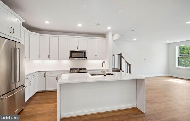 kitchen with white cabinets, sink, appliances with stainless steel finishes, and an island with sink