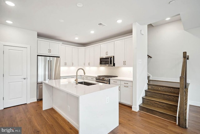 kitchen with hardwood / wood-style floors, a center island with sink, sink, premium appliances, and white cabinetry