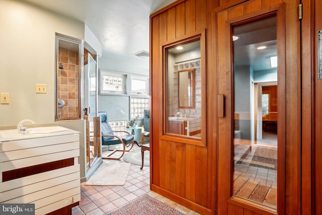 hall with wood walls, light tile patterned floors, and sink