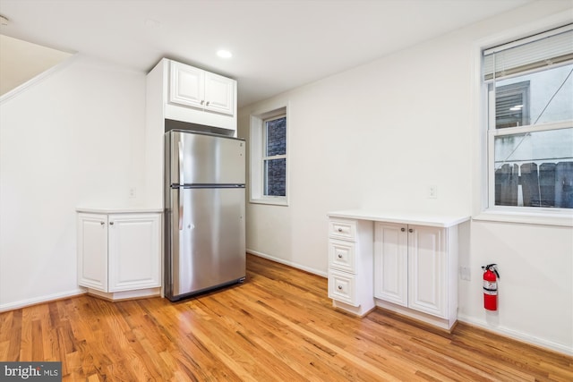 kitchen featuring baseboards, light wood-style floors, freestanding refrigerator, and white cabinets