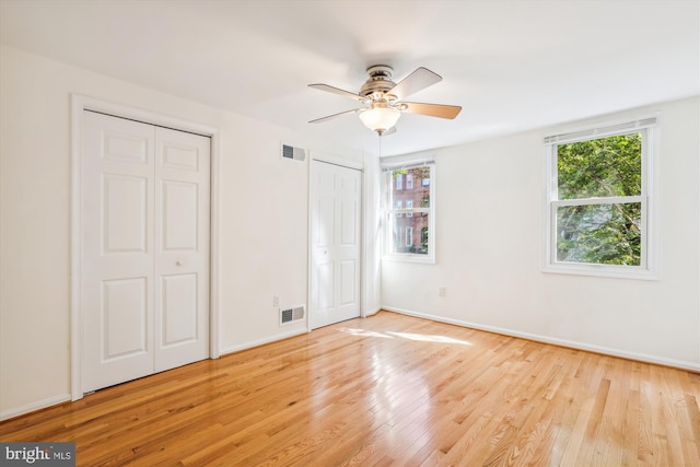 unfurnished bedroom featuring wood finished floors, visible vents, baseboards, and two closets