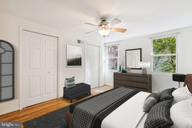 bedroom with a ceiling fan, visible vents, multiple closets, and wood finished floors