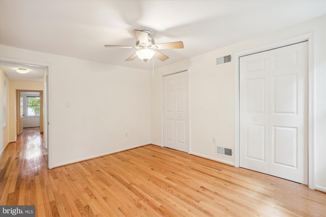 unfurnished bedroom with light wood-style floors, visible vents, ceiling fan, and two closets