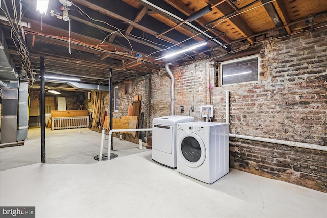 laundry room featuring heating unit, laundry area, brick wall, and washing machine and clothes dryer