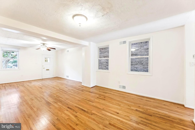 empty room featuring a textured ceiling, ceiling fan, visible vents, and light wood-style floors