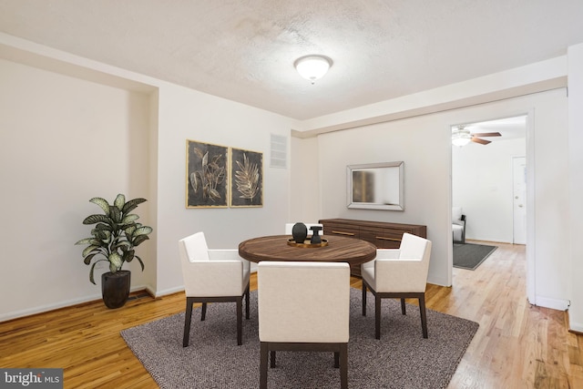 dining space with light wood-style floors, a textured ceiling, and baseboards