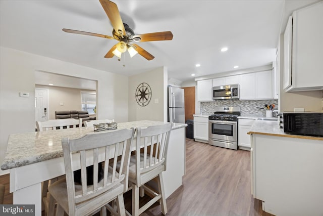 kitchen featuring a kitchen breakfast bar, tasteful backsplash, white cabinets, and stainless steel appliances