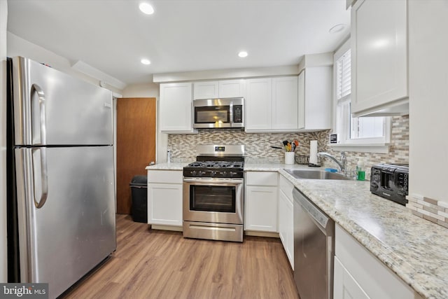 kitchen with sink, decorative backsplash, light wood-type flooring, appliances with stainless steel finishes, and white cabinetry