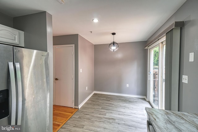 kitchen with stainless steel fridge, light wood-type flooring, white cabinetry, and hanging light fixtures