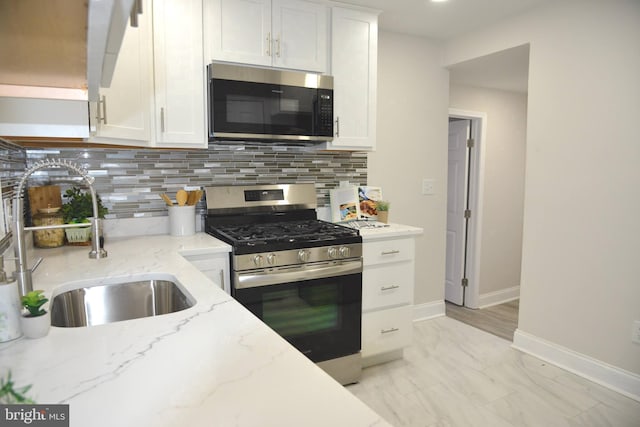 kitchen with white cabinets, stainless steel appliances, light stone counters, and sink