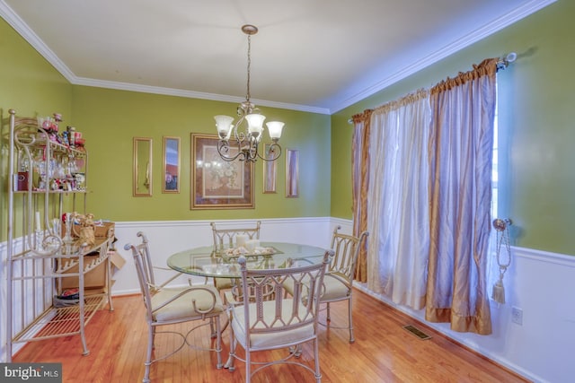 dining room with crown molding, light wood-type flooring, and an inviting chandelier