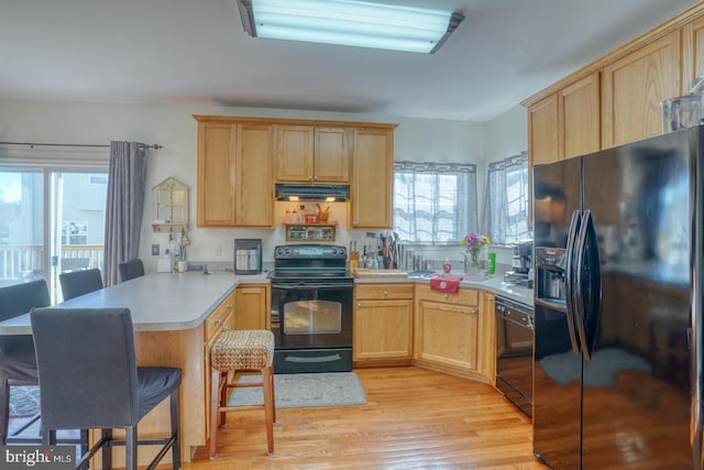 kitchen featuring kitchen peninsula, a kitchen bar, a wealth of natural light, and black appliances