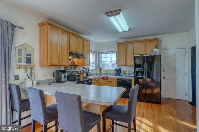 kitchen with kitchen peninsula, a kitchen bar, light hardwood / wood-style floors, and black appliances