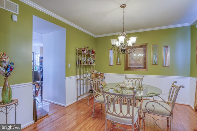 dining area featuring light wood-type flooring, ornamental molding, and an inviting chandelier