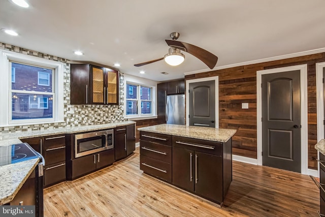 kitchen featuring light stone counters, dark brown cabinets, a kitchen island, and appliances with stainless steel finishes