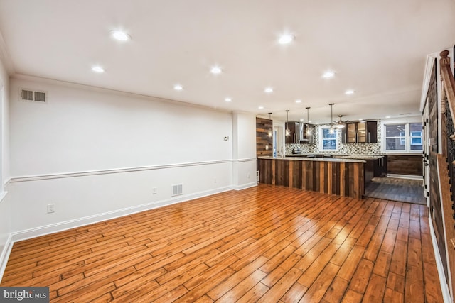 kitchen with decorative light fixtures, tasteful backsplash, light hardwood / wood-style flooring, and crown molding