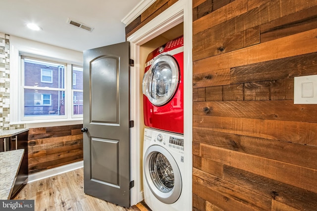 washroom with light wood-type flooring, stacked washer / dryer, and wooden walls