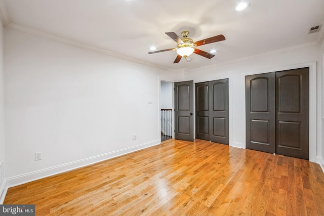 unfurnished bedroom featuring ceiling fan, two closets, crown molding, and light hardwood / wood-style flooring