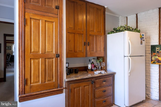 kitchen featuring white refrigerator, light stone counters, ornamental molding, and brick wall