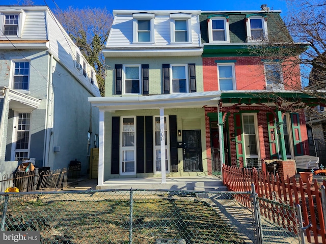 victorian home with a fenced front yard, covered porch, brick siding, and mansard roof