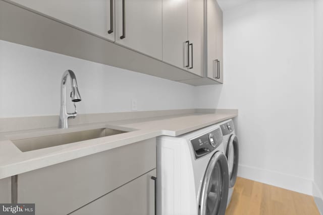 clothes washing area featuring washer and clothes dryer, sink, cabinets, and light wood-type flooring