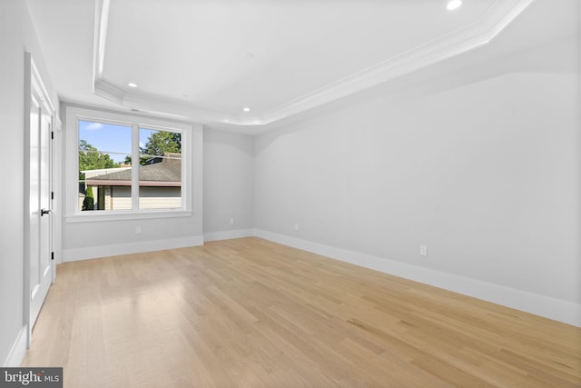 empty room with a raised ceiling, ornamental molding, and light hardwood / wood-style flooring