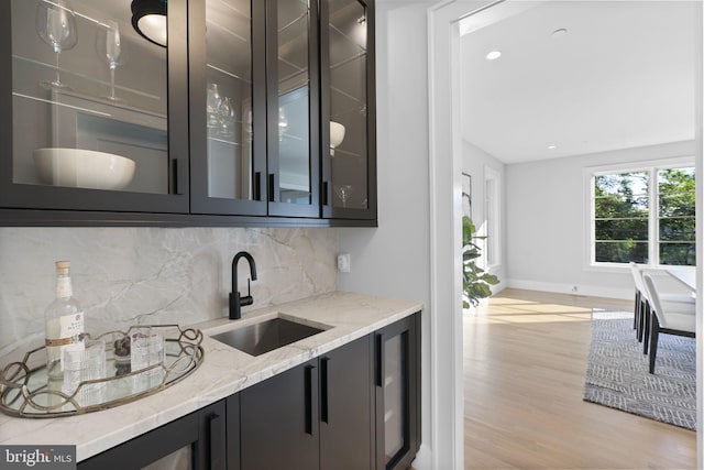 bar with light stone countertops, light hardwood / wood-style floors, tasteful backsplash, and sink