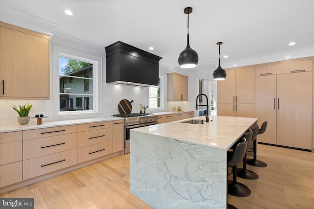 kitchen with sink, an island with sink, decorative light fixtures, light brown cabinetry, and stainless steel stove