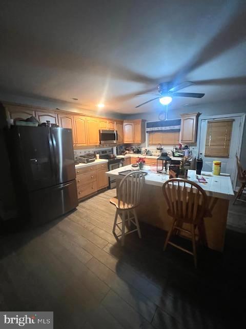 kitchen with ceiling fan, appliances with stainless steel finishes, backsplash, a kitchen breakfast bar, and light wood-type flooring